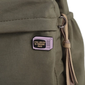 Detailed close-up of a purple forensic files TV enamel pin on a green canvas backpack