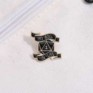 Detail shot of a black and gold D20 dice enamel pin on a white canvas bag texture