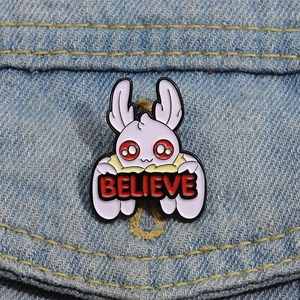 Close-up of a purple mothman enamel pin with Believe banner on blue denim fabric