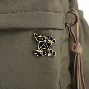 Detail of a D20 dice enamel pin on a green canvas bag with MY ROLL IN LIFE text