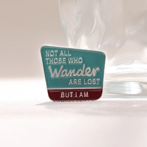 Broche en émail avec citation de voyage et bordure argentée sur fond clair minimaliste