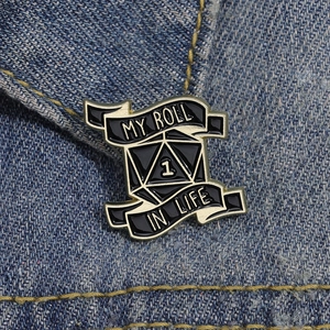 Detail of a D20 dice enamel pin on denim jacket with My Roll In Life slogan