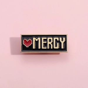 Spilla smaltata retro pixel art MERCY con cuore rosso su fondo nero per abiti