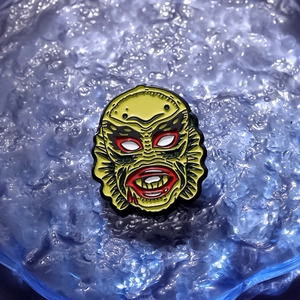 Vintage green swamp monster enamel pin with classic movie design on blue ice background