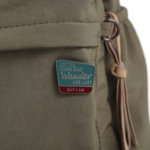 Détail macro d'une broche en émail avec texte humoristique sur un sac en nylon olive