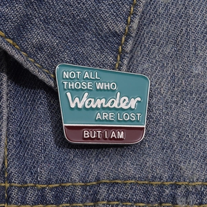 Détail d'une broche en émail sur veste en jean avec le texte Not All Those Who Wander Are Lost