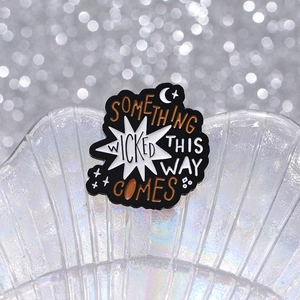 Black enamel brooch with orange Wicked text, moon and stars on a shell background