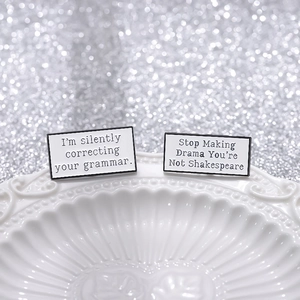 Minimalist black and white enamel letter pins with witty quotes on white ceramic plate