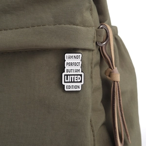 Detail of inspirational quote enamel pin accessory on an olive green canvas backpack