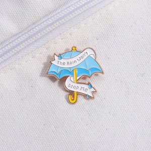 Makro-Detail der Emaille-Regenschirm-Brosche mit Motivationsspruch auf weißem Segeltuch