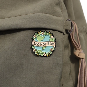 Detail of Eco Not Ego earth enamel pin attached to a green canvas backpack fabric