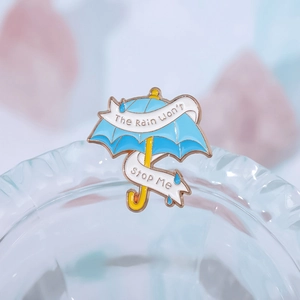 Blauer Emaille-Pin Regenschirm mit The Rain Won't Stop Me Spruch am Glasrand