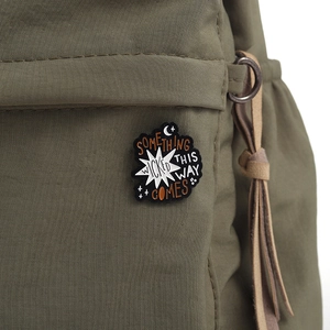 Detailed close-up of a black enamel pin on a green canvas backpack with literary text