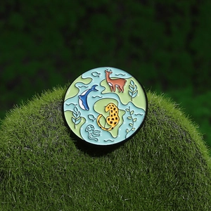 Cartoon earth enamel pin with wildlife and ocean patterns on green moss background