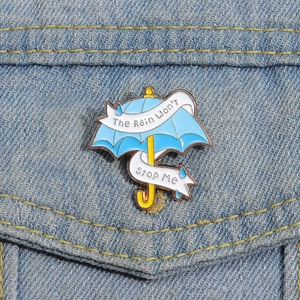 Detail der blauen Regenschirm-Emaille-Anstecknadel mit Spruch auf einer Jeansjacke