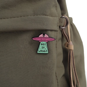 Detail of UFO enamel pin with Get In Loser slogan on olive green canvas fabric