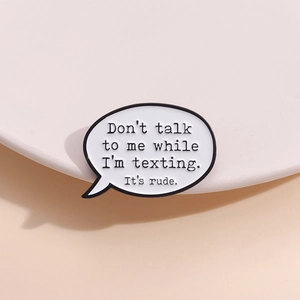 Black and white speech bubble enamel pin featuring witty English quote on white stand