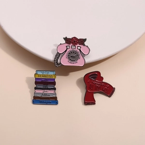 Drei Emaille-Anstecknadeln mit rosa Telefon, rotem Schal und Stapel von Album-Büchern