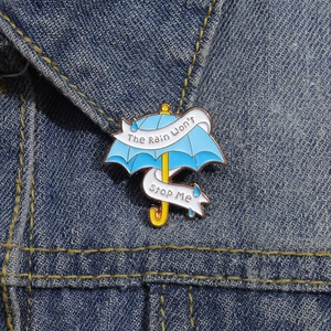 Dettaglio della spilla a ombrello blu con testo motivazionale su tessuto in denim