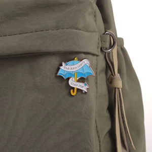 Dettaglio della spilla a ombrello blu con scritta su una borsa di tela verde scuro