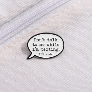 Detail of enamel pin with quote Don't talk to me while I'm texting on white canvas fabric