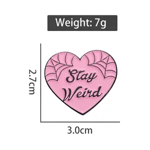 Pink heart enamel pin with Stay Weird text and spider web pattern on white background