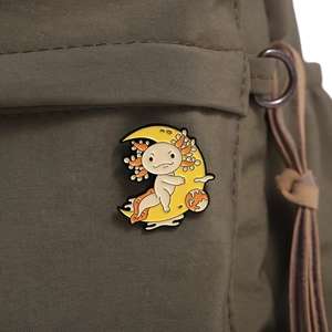 Macro detail of cartoon axolotl enamel pin with moon on a brown nylon backpack