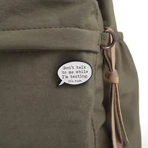 Detail of an enamel quote brooch on a green canvas backpack showing texting dialogue design