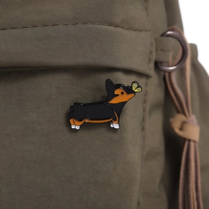 Nahaufnahme einer Corgi-Emaille-Anstecknadel mit Schmetterling auf grünem Stoff