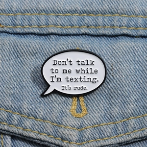 Détail d'un pin's émaillé bulle de texte blanche sur une veste en jean bleu clair