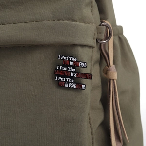 Detailed view of an enamel pin with sarcastic quote on an olive canvas backpack