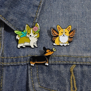 Detailansicht von drei süßen Corgi-Emaille-Pins mit Flügeln auf blauem Denim-Stoff