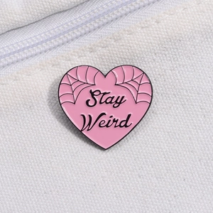 Pink heart enamel pin with Stay Weird text and spider web pattern on white canvas bag