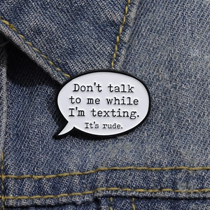 Close-up of a comic speech bubble enamel pin on blue denim fabric with funny text