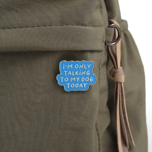 Gros plan d'une broche en émail bleu avec message humoristique sur tissu vert olive
