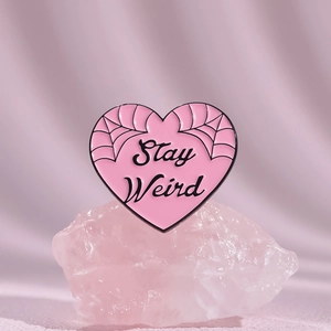 Pink heart enamel pin with Stay Weird text and spider web design on a pink crystal base