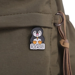 Detail of penguin enamel pin with 'MORE SPRINKLES PLEASE!' text on a green canvas bag