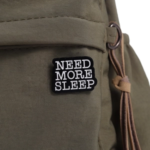 Macro shot of black enamel 'NEED MORE SLEEP' slogan badge pinned on green canvas bag
