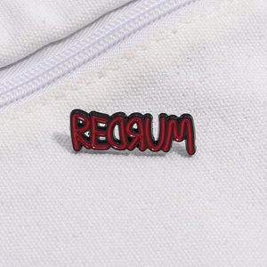 Macro view of REDRUM enamel brooch pin on white canvas background with zipper detail