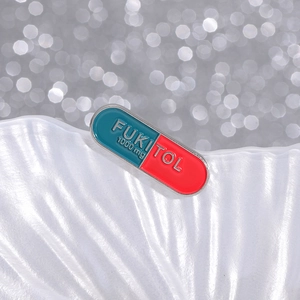 Blue and red capsule enamel pin with FUKITOL 1000mg text on white wave tray