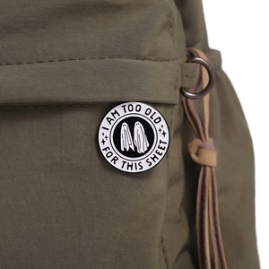 Detail einer runden Geister-Emaille-Anstecknadel auf einer grünen Tasche mit Text