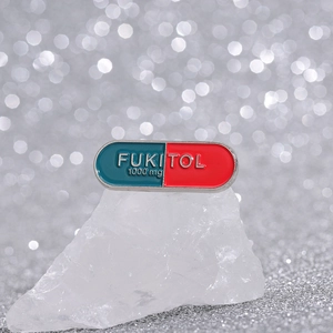 Funny FUKITOL pill-shaped enamel pin in red and teal colors with silver lettering