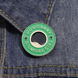 Gros plan d'un pin's émaillé vert Honorary Gilmore Girl sur une veste en jean bleue
