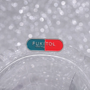 Humorous pill capsule enamel brooch with FUKITOL text on transparent glass edge