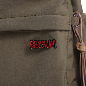 Close-up of a red REDRUM enamel pin attached to a green fabric bag with D-ring detail