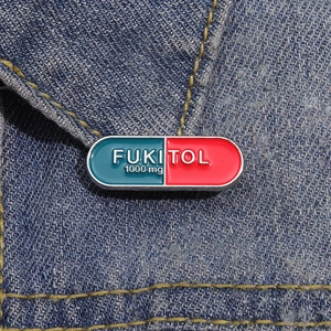 Close-up of red and blue capsule enamel pin with FUKITOL text on blue denim fabric