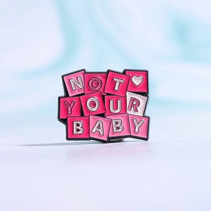 Emaille-Pin in Rosa mit NOT YOUR BABY Schriftzug und weißem Herz auf schwarzem Metall