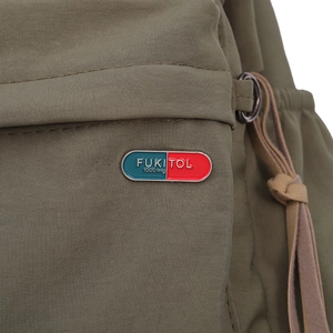 Detail of red and blue capsule badge with FUKITOL text on olive green canvas bag