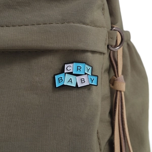 Detailed shot of Cry Baby enamel pin on an olive green canvas bag with leather tassel
