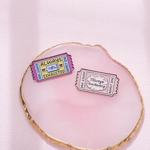 Enamel pins shaped like cinema tickets featuring Always Exhausted and Overthinking text